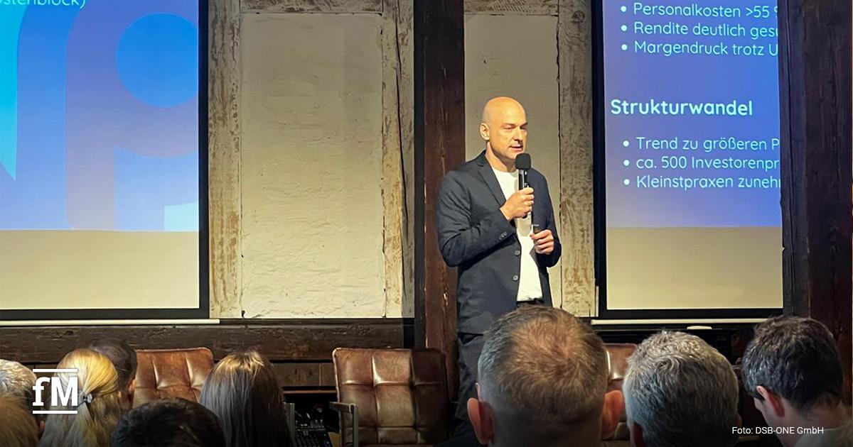 Ein Mann mit Mikrofon steht vor einer Leinwand mit der Überschrift „Physiotherapie Wirtschaftlichkeit“. Im Vordergrund sitzen Zuhörer.