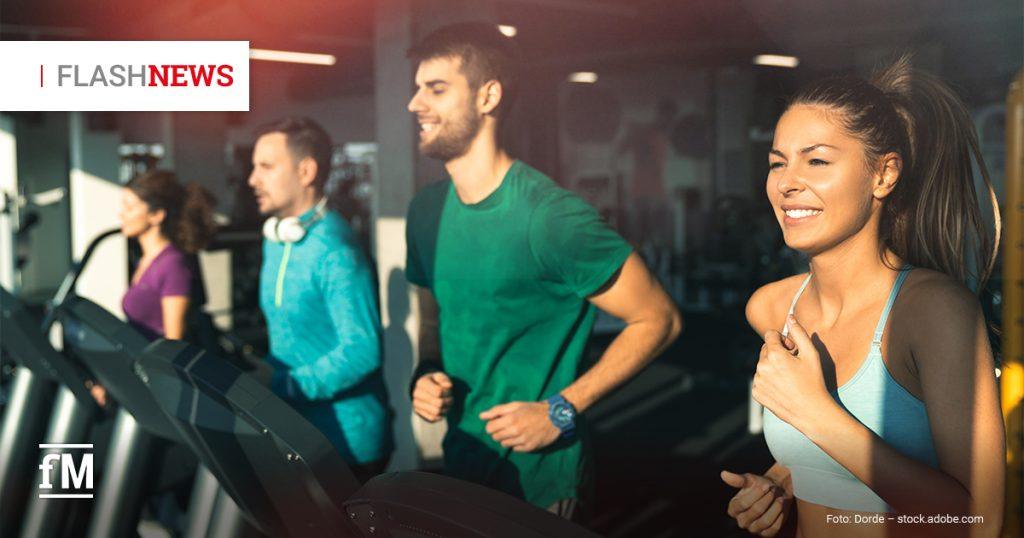Vier Personen laufen auf Laufbändern in einem Fitnessstudio; im Vordergrund lächelt eine Frau im hellblauen Sporttop, oben links steht „FLASHNEWS“.
