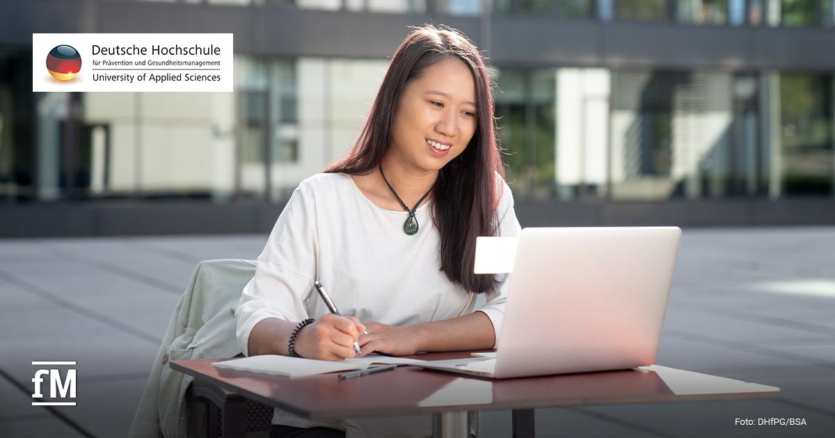DHfPG Sport- und Bewegungstherapie Im Vordergrund sitzt eine Person an einem Tisch vor einem Laptop und schreibt in ein Notizbuch. Links oben steht das Logo mit dem Text „Deutsche Hochschule für Prävention und Gesundheitsmanagement University of Applied Sciences“. Links unten steht das fM-Logo, rechts unten der Text „Foto: DHfPG/BSA“.