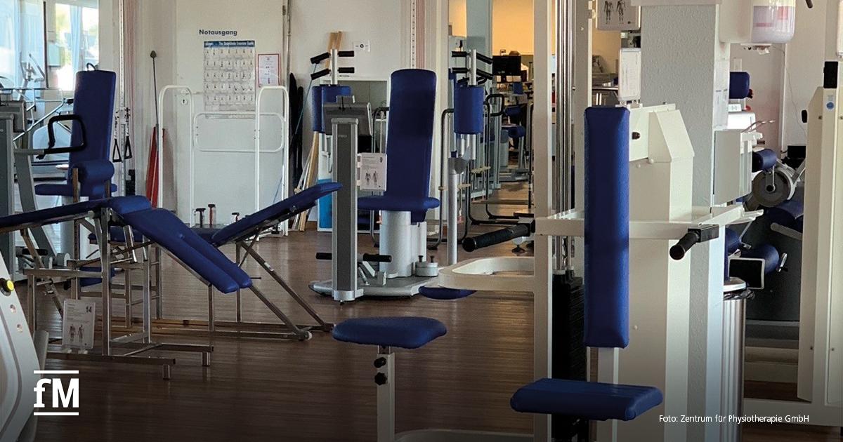 Trainingsfläche mit mehreren Kraftgeräten, blauen Polstern und Therapieliegen in einem hellen Raum mit Holzfußboden.