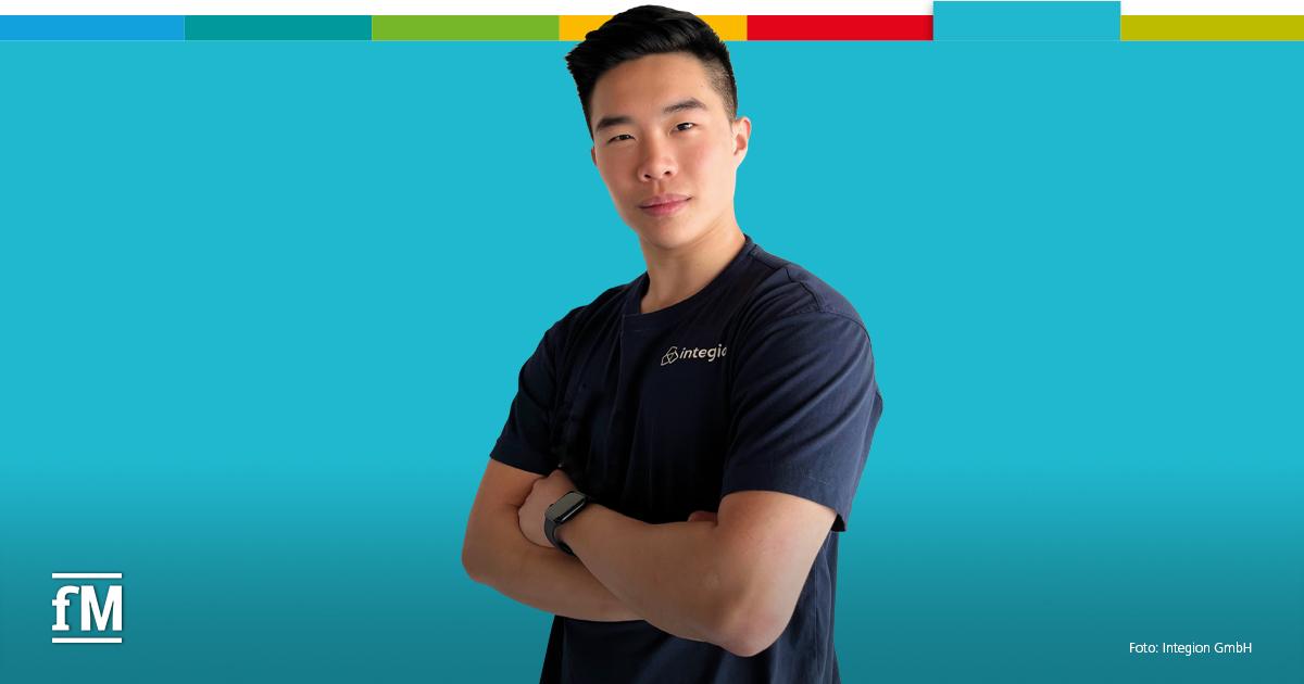 DHfPG Absolvent Hung Quang Nguyen Hung Quang Nguyen steht frontal mit verschränkten Armen vor türkisem Hintergrund. Er trägt ein dunkles T-Shirt mit Integion-Logo auf der linken Brust. Oben verläuft ein mehrfarbiger Balken.