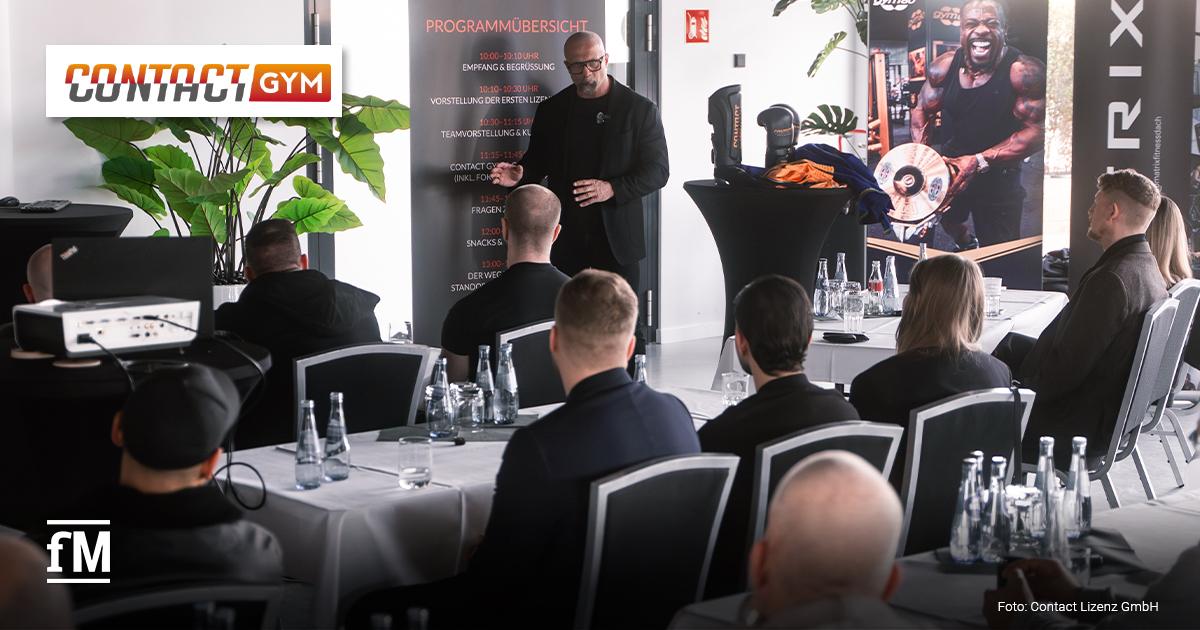 Contact Lizenz GmbH Meet and Greet 2026 Im Vordergrund sitzen Teilnehmende an gedeckten Konferenztischen. In der Bildmitte spricht eine Person vor einem Aufsteller mit der Überschrift „PROGRAMMÜBERSICHT“. Rechts stehen ein Stehtisch mit Kampfsportausrüstung, ein Banner mit Athletenmotiv und ein vertikales Logo von Matrix Fitness. Im Hintergrund sind Pflanzen, Fensterflächen und weitere Sitzplätze sichtbar.