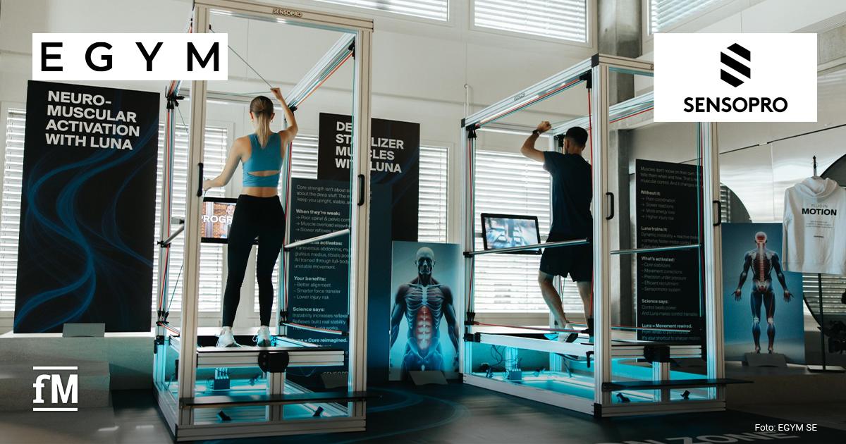 EGYM Sensopro Integration Trainingsraum mit zwei Personen in Sensopro-Trainingsrahmen, links eine Person von hinten an Widerstandsbändern, rechts eine Person von hinten an einem Trainingsrahmen mit Bildschirm im Vordergrund. Oben links steht das Logo „EGYM“, oben rechts das Logo „SENSOPRO“. Unten links steht das Logo „fM“, unten rechts die Bildquelle.