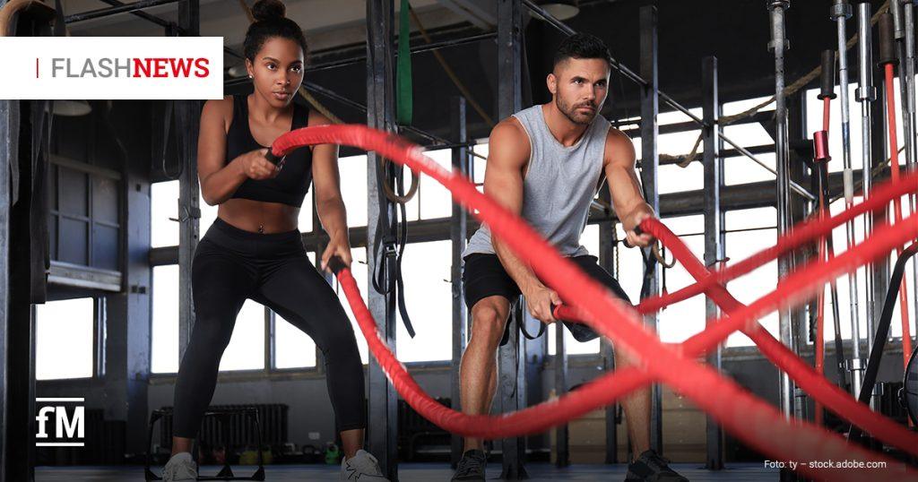 Zwei Personen trainieren in einem Fitnessstudio mit roten Battle Ropes. Sie stehen in leichter Kniebeuge und schwingen die Seile kraftvoll vor sich. Oben links steht „FLASH NEWS“, unten links das fM-Logo.