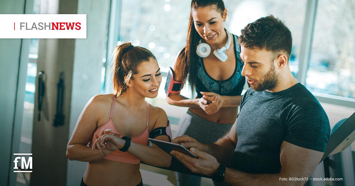 Fitness Flash News #06/2026 KW 26 Zwei Trainierende und ein Trainer in einem Fitnessstudio betrachten gemeinsam ein Tablet; eine Frau prüft ihre Smartwatch, während ein Mann die Trainingsdaten zeigt. Oben links eingeblendet: „FLASH NEWS“.