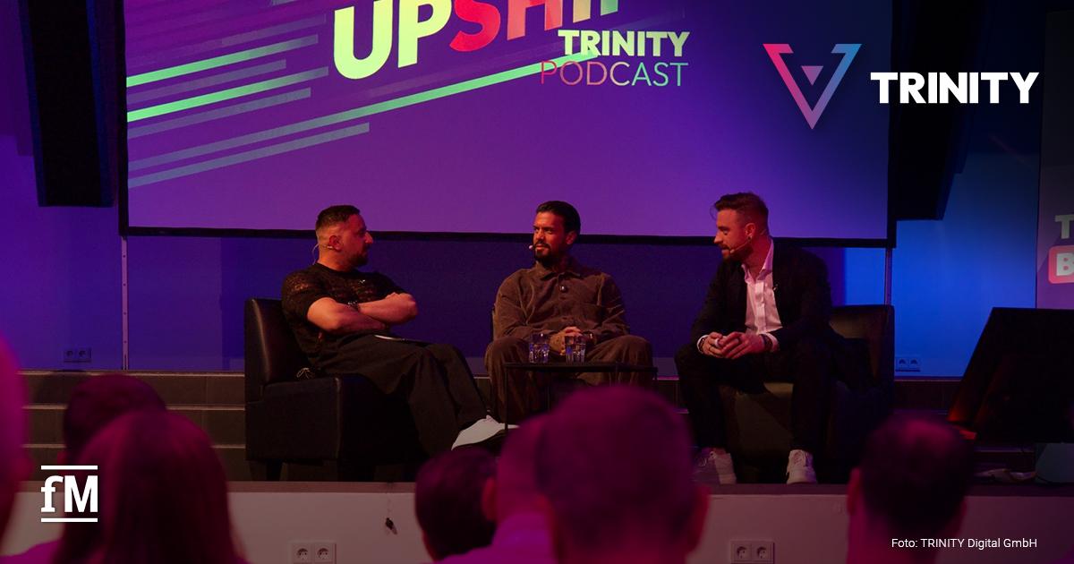 TRINITY: THE NEXT BIG THING Drei Männer sitzen auf einer Bühne in schwarzen Sesseln und sprechen miteinander.