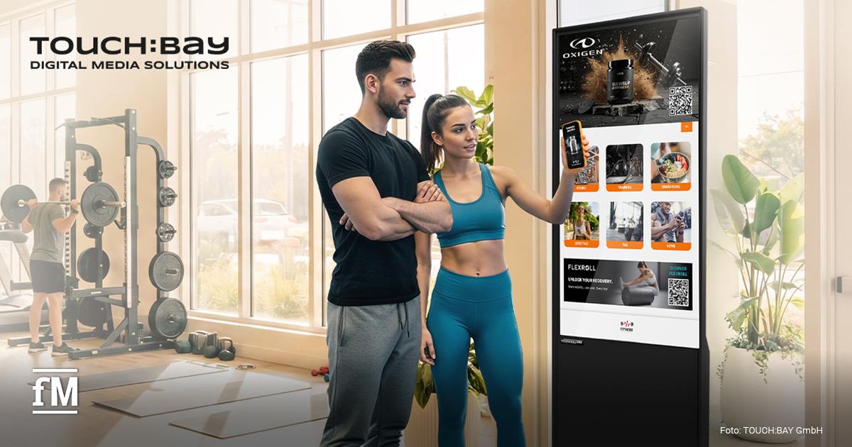 TOUCH:BAY Werbeplattform Zwei Fitnessstudiomitglieder bedienen einen digitalen TOUCH:BAY-Touchscreen im Trainingsbereich.
