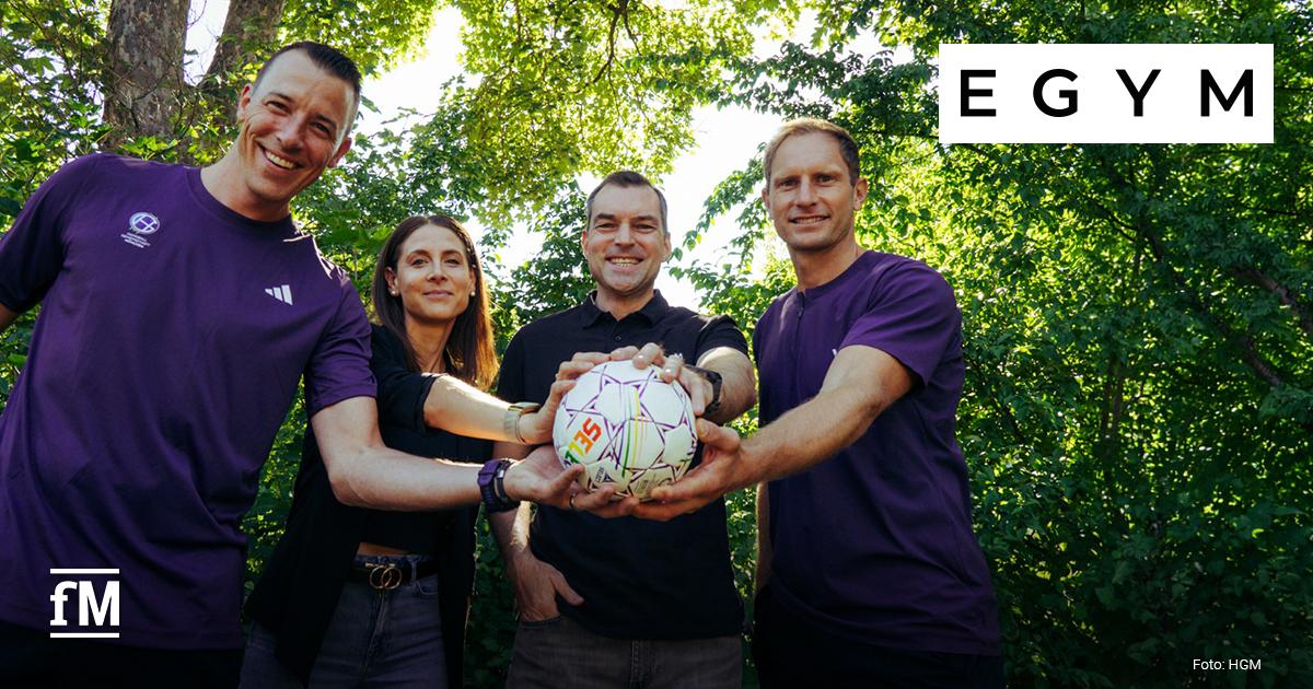 EGYM Partnerschaft Handballgemeinschaft München (HGM) Vier Personen halten gemeinsam einen Handball im Freien. Rechts oben ist das EGYM-Logo zu sehen.