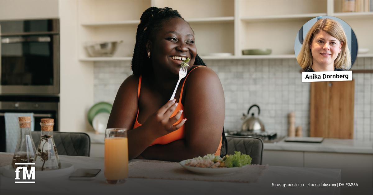 Mindful Eating Frau sitzt lächelnd mit einer Gabel und einem Teller Salat am Esstisch; Porträt von Annika Dornberg eingeblendet