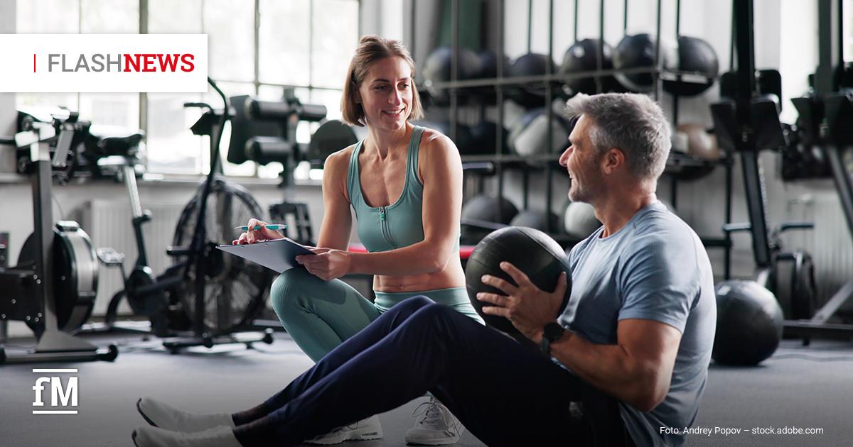 Fitness Flash News 07/2026 KW 30 Trainerin berät einen Trainierenden im Fitnessstudio während einer Übung mit einem Medizinball.