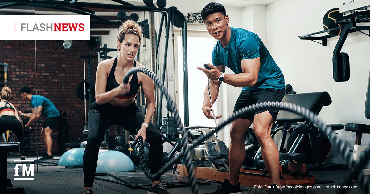Fitness Flash News #0772026 KW 31 Trainer betreut eine Frau beim Training mit Battle Ropes in einem Fitnessstudio. Im Hintergrund sind weitere Trainingsgeräte und trainierende Personen zu sehen.