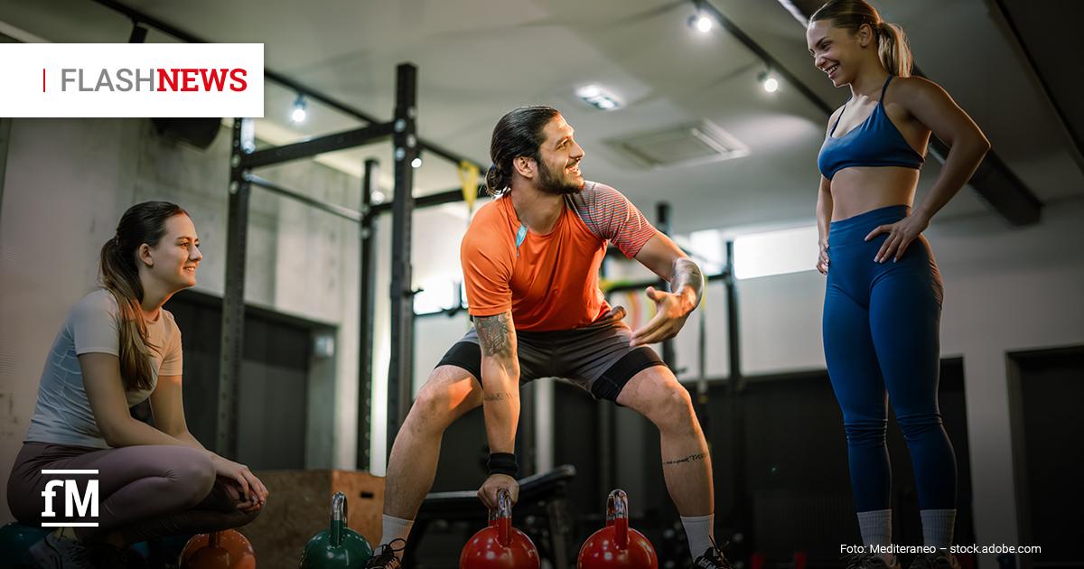 Fitness Flash News #08/2026 KW32 Drei Personen in einem Fitnessstudio: Eine Person hebt zwei Kettlebells an, während zwei weitere lächelnd daneben stehen bzw. sitzen und das Training beobachten. Oben links ist der Schriftzug „FLASHNEWS“ eingeblendet.