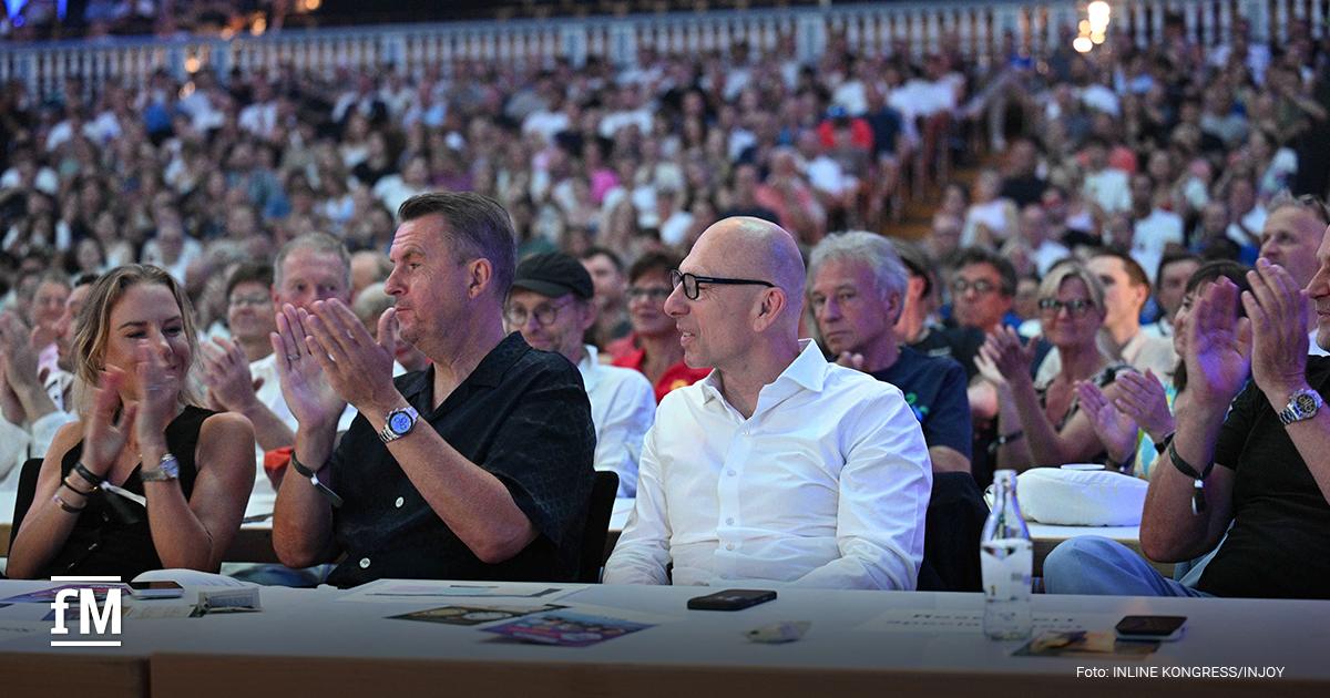 Publikum sitzt an Tischen und applaudiert in einem voll besetzten Veranstaltungssaal.