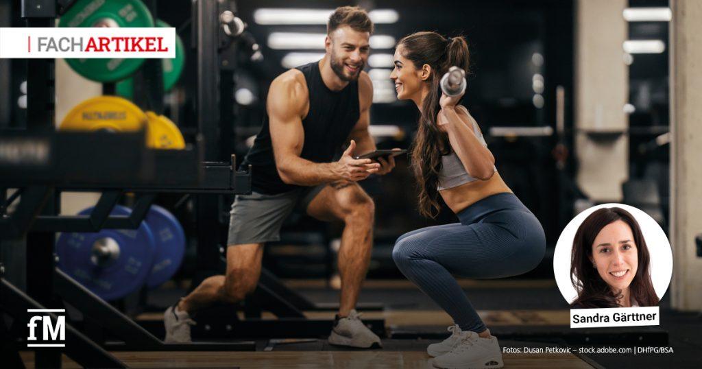 Trainer begleitet eine Trainierende beim Krafttraining mit Kurzhanteln im Fitnessstudio.