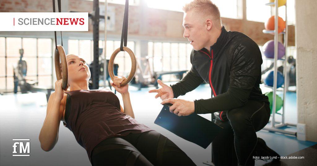 Trainer betreut eine Trainierende an Turnringen in einem Fitnessstudio und gibt Gesundheitstipps.