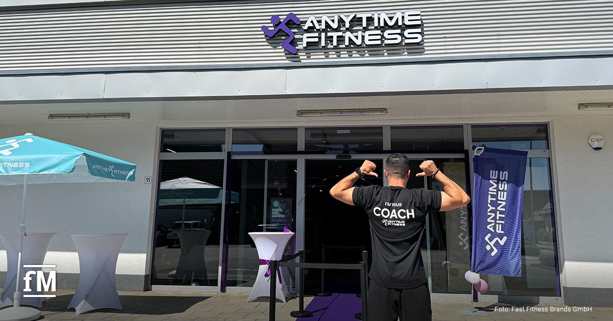 Eingang eines Anytime-Fitness-Studios mit Logo und Mitarbeiter auf violettem Teppich