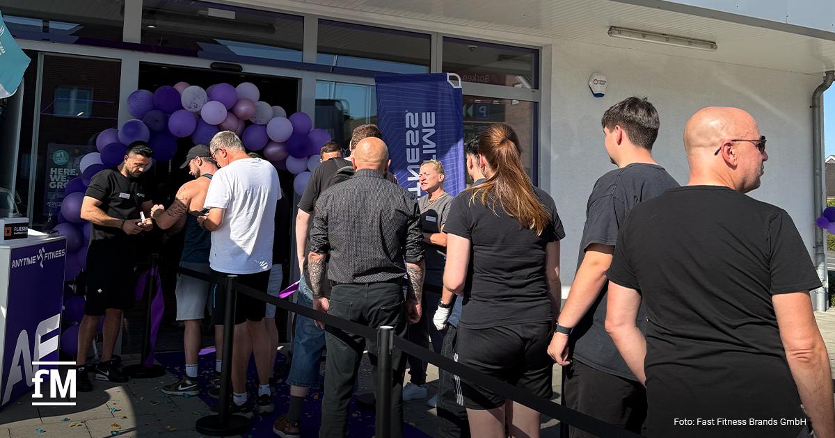 Besucher stehen vor dem Eingang eines Anytime-Fitness-Studios auf einem violetten Teppich