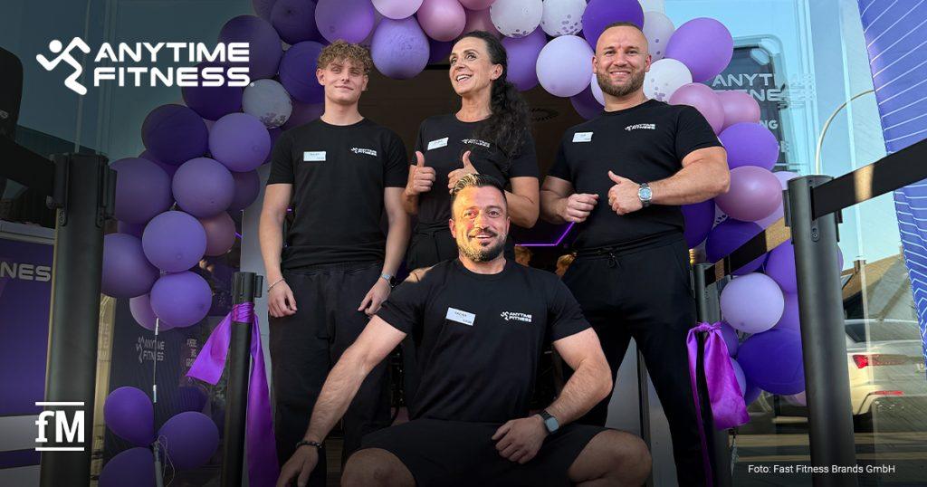 Vier Personen in Anytime-Fitness-Shirts vor einem violetten Ballonbogen am Studioeingang.
