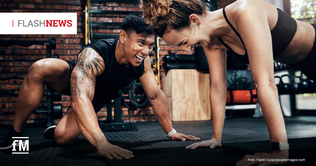 Fitness Flash News #08/2026 KW 34 Ein lachender Trainer und eine Frau in Sportkleidung stützen sich beim Training auf einer Matte ab. Oben links steht „FLASH NEWS“.