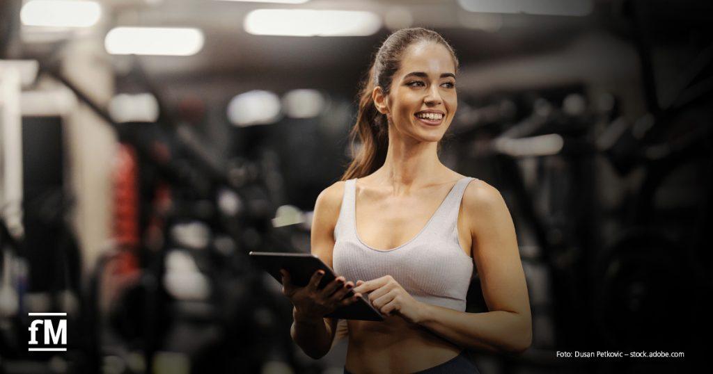 Frau mit Tablet zwischen Trainingsgeräten in einem Fitnessstudio.