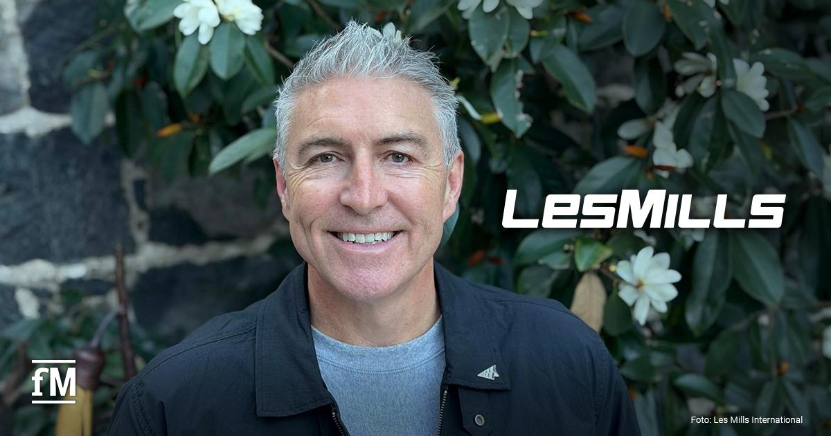 Jason Paris CEO neuer CEO Les Mills International Jason Paris vor grüner Bepflanzung, daneben das weiße Logo von Les Mills