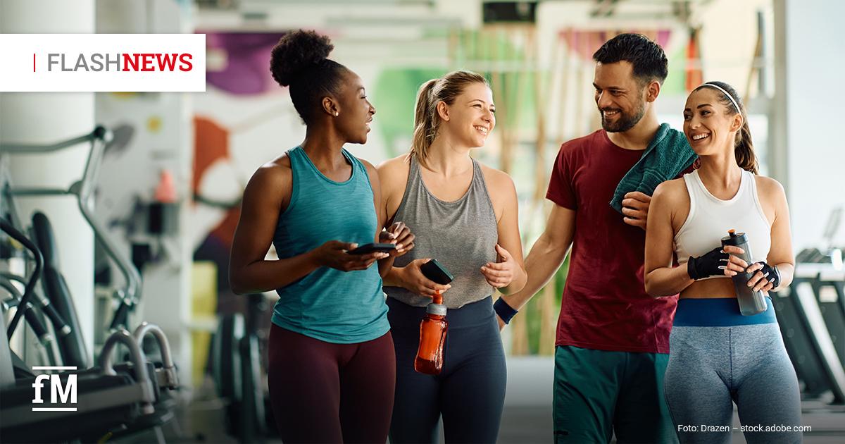 Fitness Flash News #09/2026 KW 38 Vier lachende Personen in Sportkleidung stehen nach dem Training gemeinsam in einem Fitnessstudio. Zwei halten Trinkflaschen. Oben links steht „FLASHNEWS“.