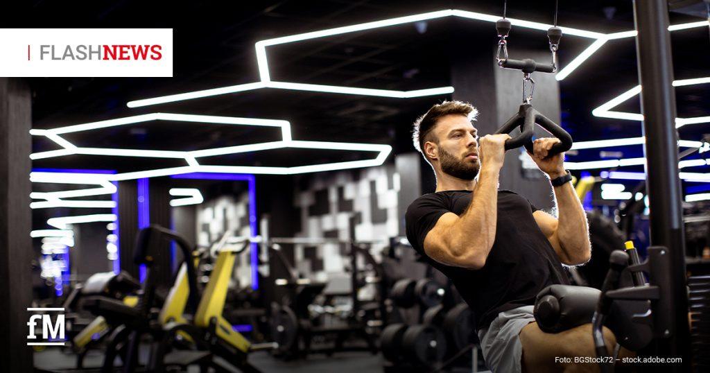 Mann trainiert an einem Kabelzug in einem Fitnessstudio mit moderner Beleuchtung.