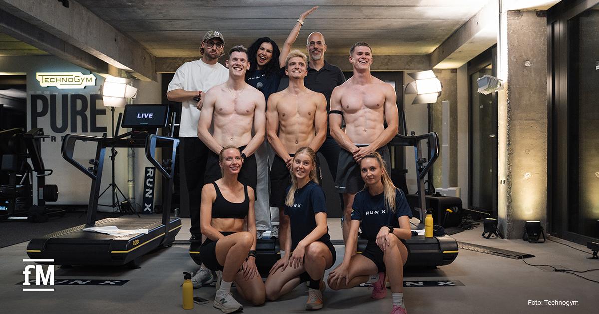 Neun Personen posieren gemeinsam vor mehreren Technogym-Laufbändern in einem Veranstaltungsraum