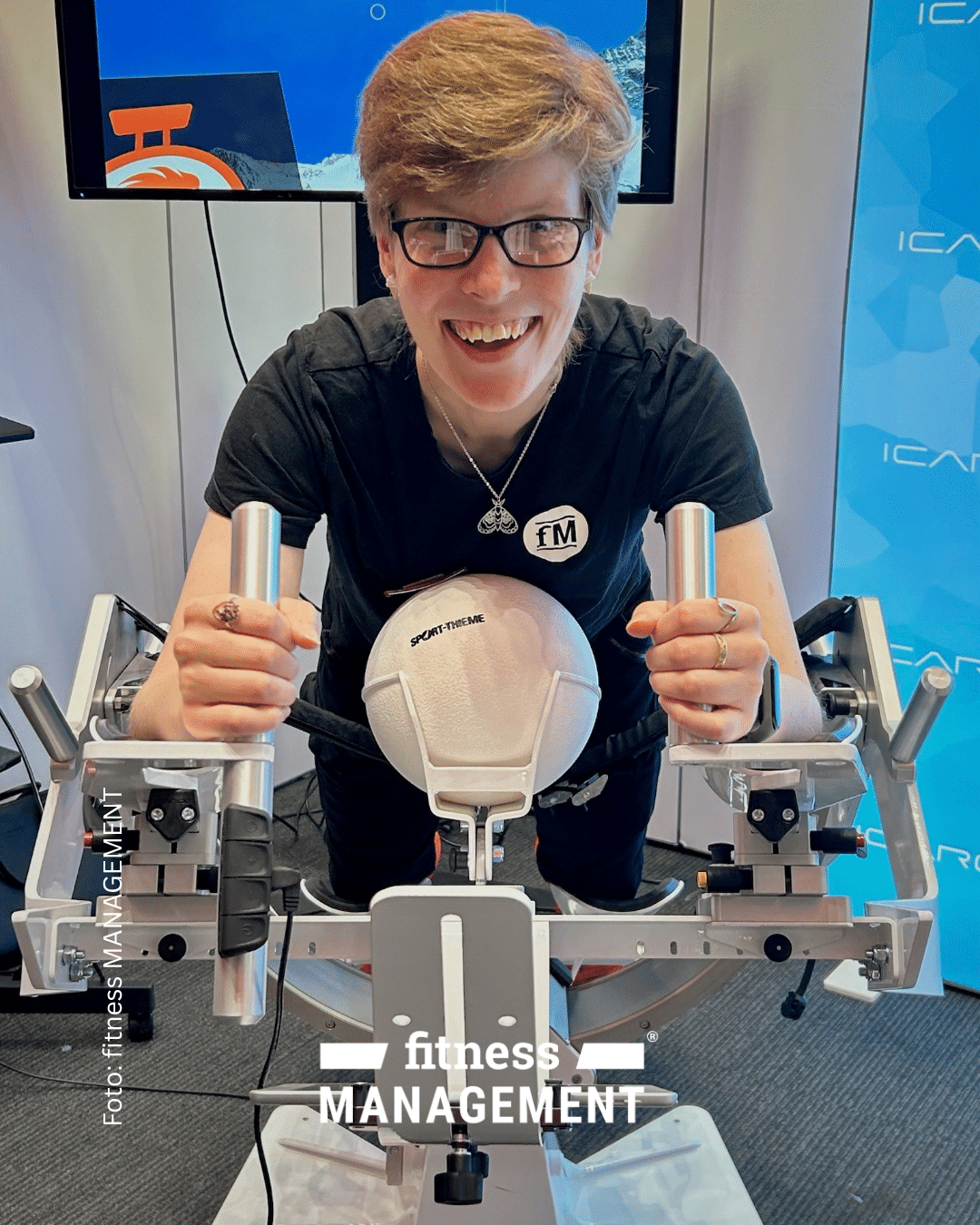 Lächelnde Person mit Brille testet ein Trainingsgerät von Sport-Thieme und hält dabei zwei Metallgriffe fest.