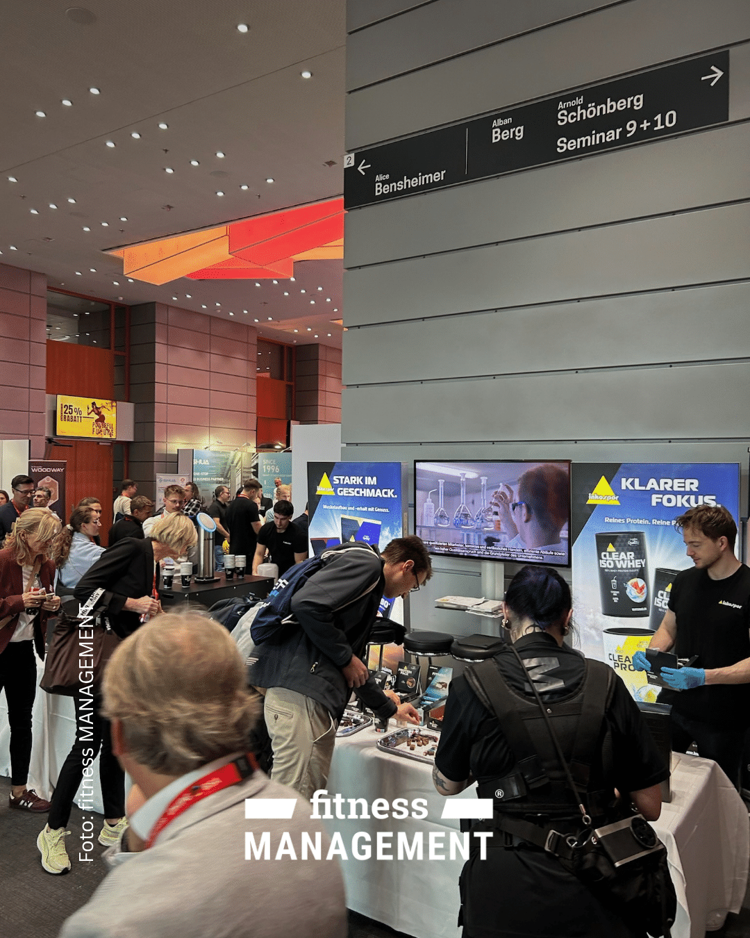 Besucherinnen und Besucher stehen an mehreren Ausstellungsständen für Sporternährung. Im Vordergrund werden Produkte präsentiert und Kostproben angeboten.