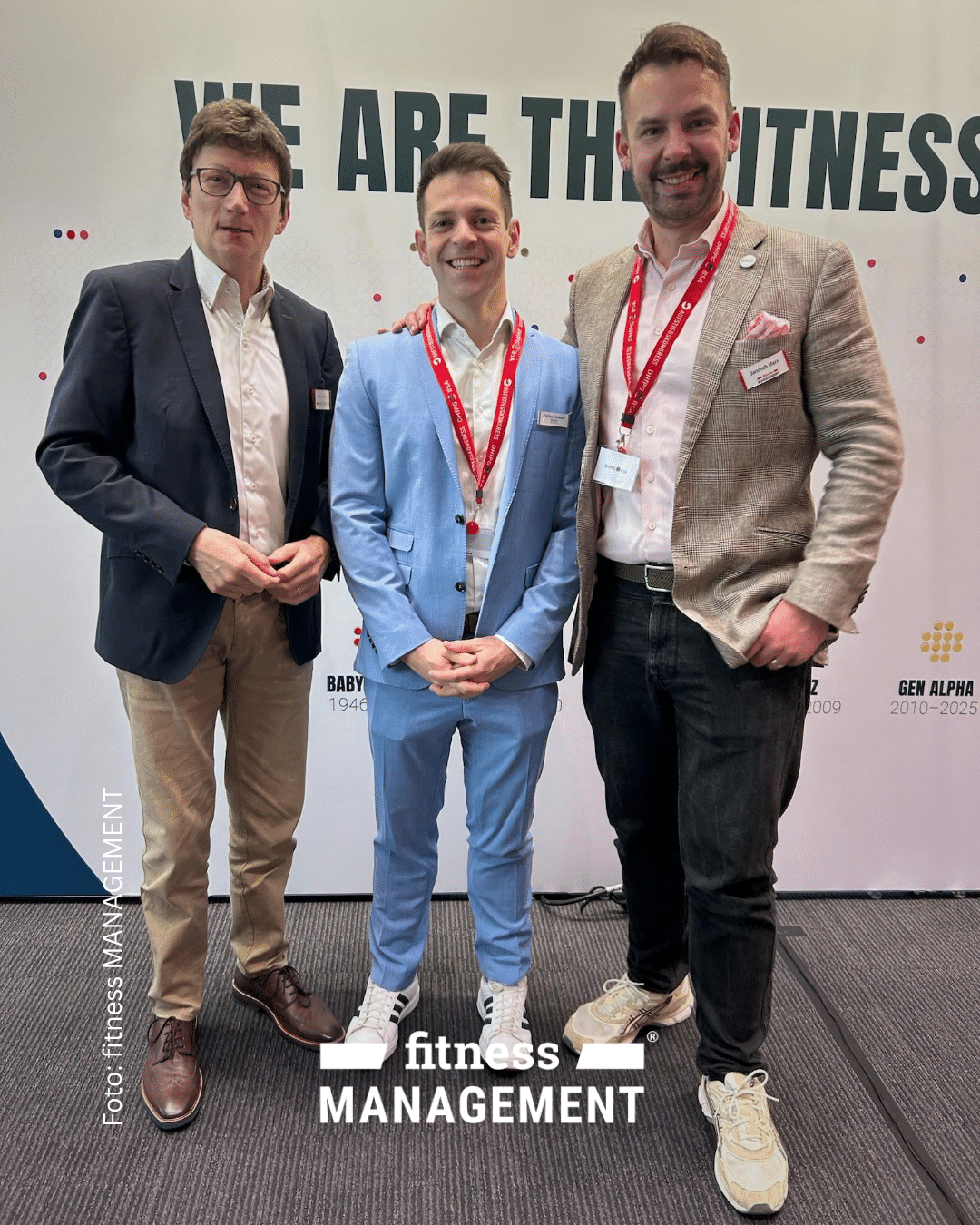 Drei Männer in Businesskleidung posieren beim Aufstiegskongress 2026 vor einer Fotowand mit dem Schriftzug „WE ARE THE FITNESS“.
