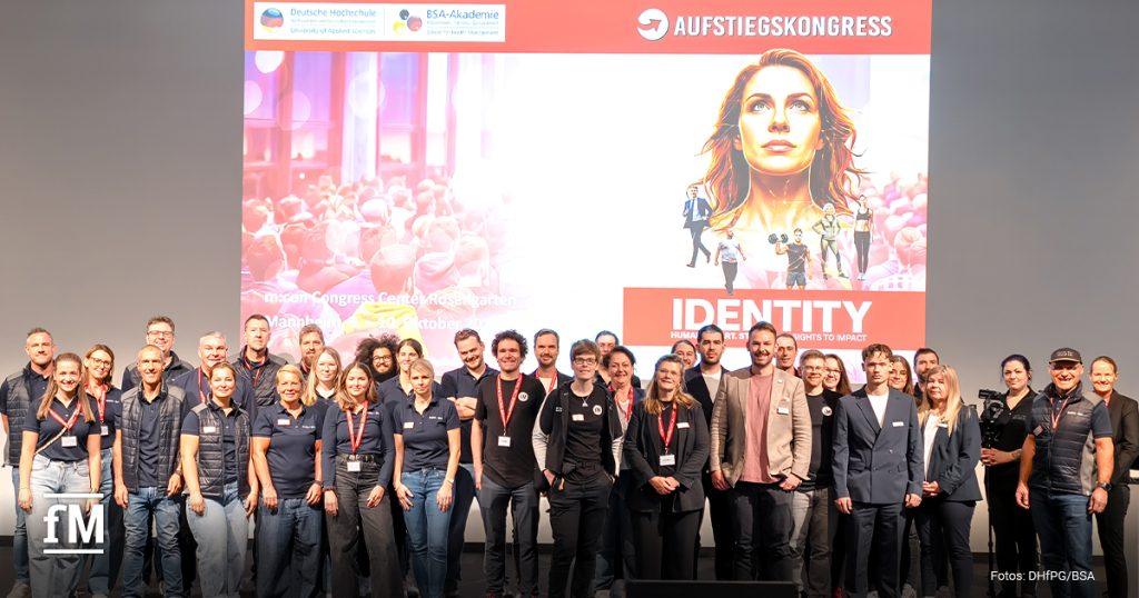 Gruppenfoto mit rund 30 Personen vor der Bühne des Aufstiegskongresses mit großem Veranstaltungsbanner im Hintergrund.