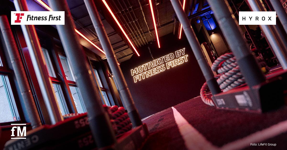 Fitness First HYROX Training Club Trainingsbereich mit Seilen, roten Lichtstreifen und beleuchtetem Fitness-First-Schriftzug.