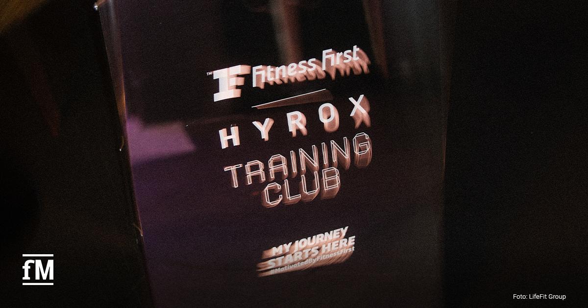 Beleuchteter Schriftzug „Fitness First HYROX Training Club“ auf einer dunklen Wand