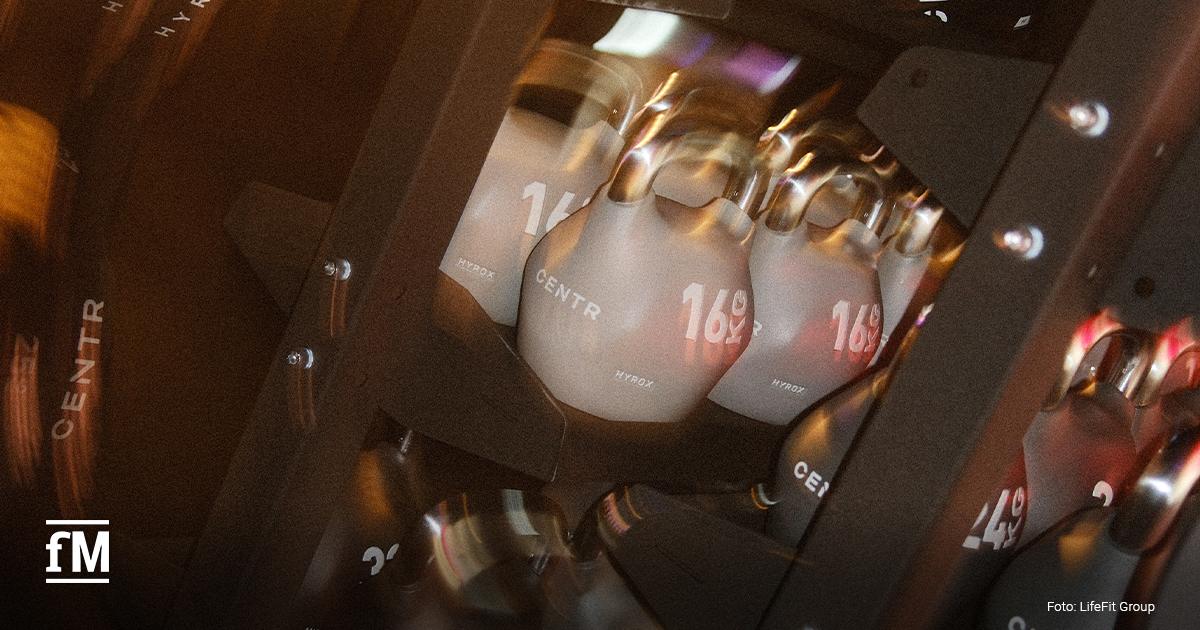 Mehrere graue HYROX-Kettlebells mit Gewichtsangaben stehen in einem schwarzen Metallregal