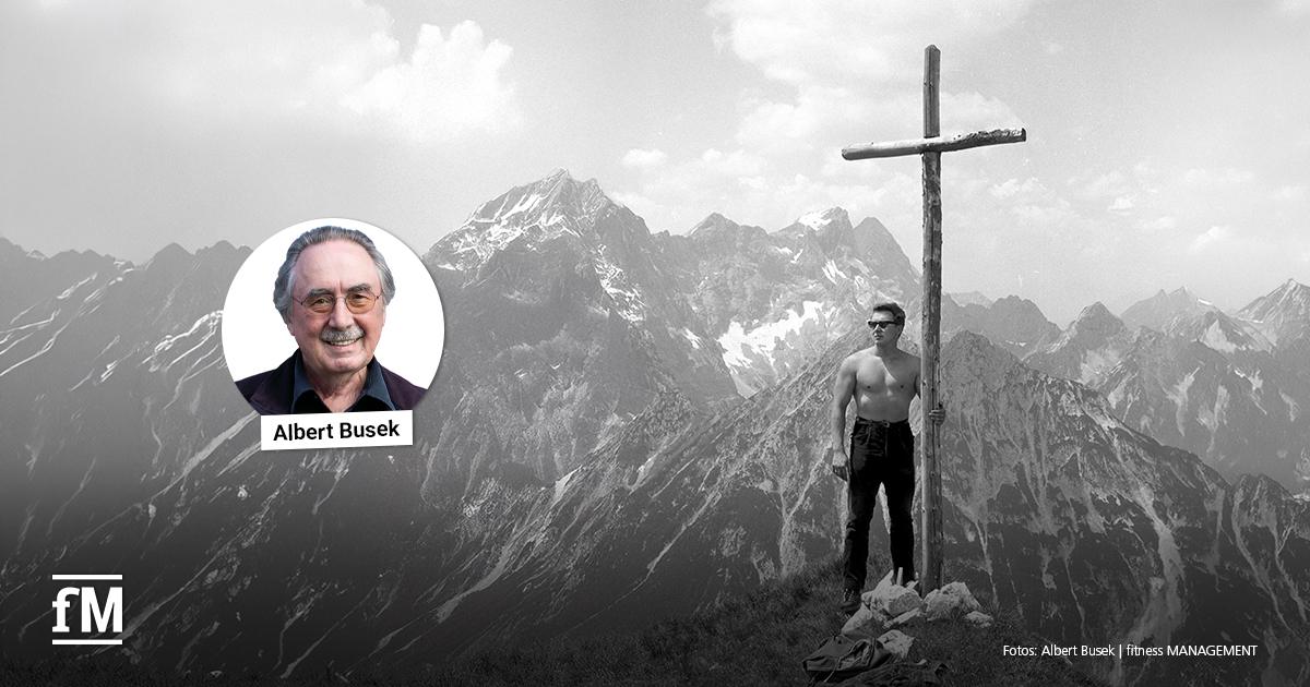 Kolumne Albert Busek Schwarz-Weiß-Aufnahme eines Mannes neben einem Gipfelkreuz in den Bergen, ergänzt um ein rundes Porträt von Albert Busek.