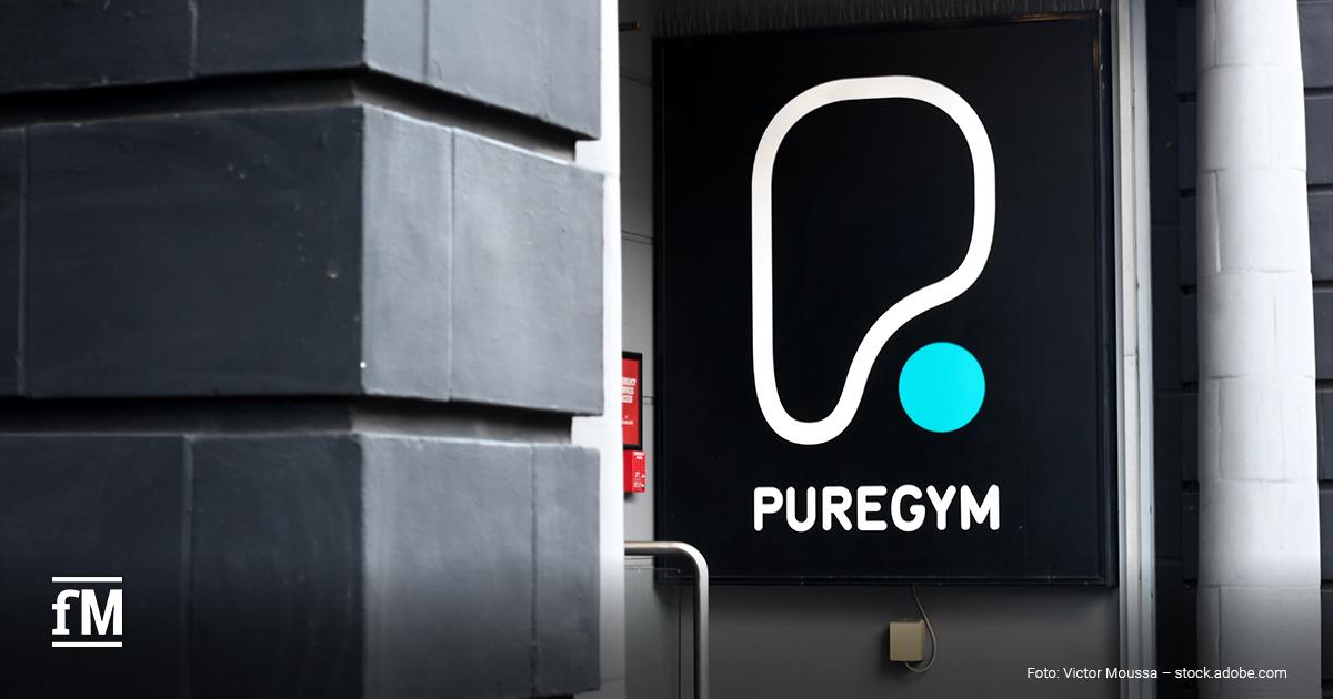 PureGym übernimmt NonStop Gym Weißes PureGym-Logo mit türkisfarbenem Punkt auf einer schwarzen Werbetafel am Gebäudeeingang.