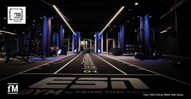 Modern ausgestatteter Functional-Training-Bereich mit Sprintbahn und weißem Schriftzug 'ESN GYM by PRIME TIME fitness', Fitnessgeräten und dunkler, lilablauer Studiobeleuchtung.