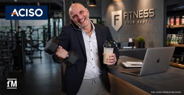 ann in einem Fitnessstudio hält eine Hantel und einen Shaker vor einem Tresen