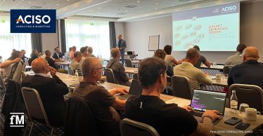 Teilnehmende eines ACISO Sommer-Netzwerktreffens in Leipzig sitzen in einem Konferenzraum und hören Thomas Taimer, ACISO Consultant, zu, der vor einer Leinwand mit der Präsentation „Zukunft gemeinsam denken“ spricht.