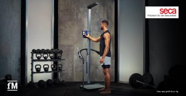 Sportler steht barfuß in einem Fitnessstudio an einer seca TRU und bedient das Display.