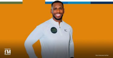 Lächelnder Mann in weißem Sportoberteil vor orangefarbenem Hintergrund mit fM-Logo.
