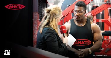 Eine Redakteurin von fitness MANAGEMENT interviewt den Bodybuilder Neckzilla an einem Panatta-Messestand. Im Hintergrund sind Trainingsgeräte zu sehen.