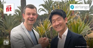 Riccardo Christ (links) und Chang-Hun Jo geben sich freundschaftlich die Hand. Christ trägt ein graues Sakko, Chang-Hun Jo ein schwarzes Sakko mit weißem Hemd. Oben links ist das Logo von clever fit, oben rechts das airtango-Logo.