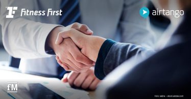 Zwei Personen im Businessumfeld geben sich über einem Tisch die Hand. Im Bild sind die Logos von Fitness First und airtango zu sehen