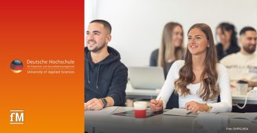 Im Vordergrund sitzen mehrere Personen an weißen Tischen in einem hellen Seminarraum; mittig hält eine Frau in weißem Oberteil einen Stift an einem Notizbuch, links sitzt ein Mann im schwarzen Hoodie, rechts liegt ein aufgeschlagenes Buch; im Hintergrund befinden sich drei unscharfe Personen und ein Laptop. Links auf rot bis gelbem Farbverlauf das Logo der Deutschen Hochschule für Prävention und Gesundheitsmanagement (DHfPG).