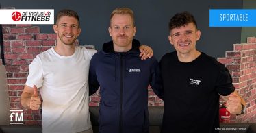 Drei junge Männer (Patrick Elbl, Nico Miller, Dominik Elbl) stehen lächelnd nebeneinander in einem Fitnessstudio vor einer Wand mit dem Logo 'all inclusive Fitness'.