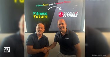 Zwei Männer sitzen vor einer Leinwand mit den Logos von Fitness Future und all inclusive Fitness und geben sich die Hand.