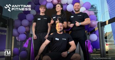Vier Personen in Anytime-Fitness-Shirts vor einem violetten Ballonbogen am Studioeingang