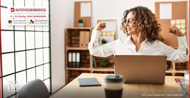 Frau sitzt am Laptop im Büro und hebt lächelnd beide angewinkelten Arme
